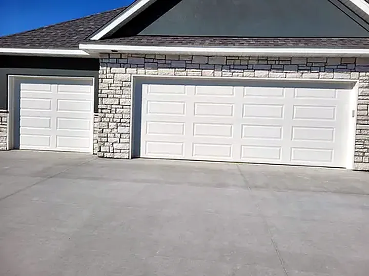 Two white raised-panel garage doors on a new stone-front home