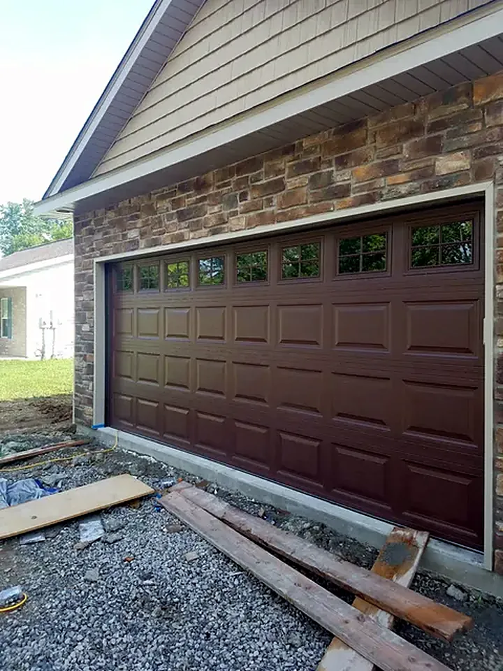Brown raised-panel garage door with windows on a stone home